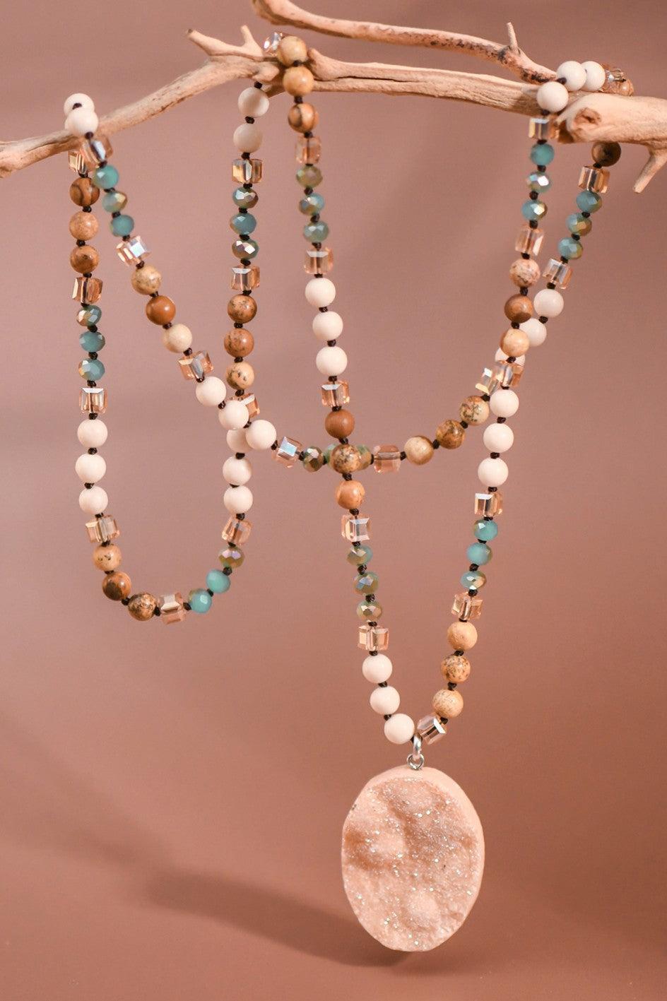 Necklace with beads and a large pendant on a branch against a brown background