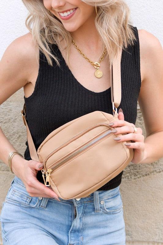 Woman holding a beige crossbody bag with a neutral background