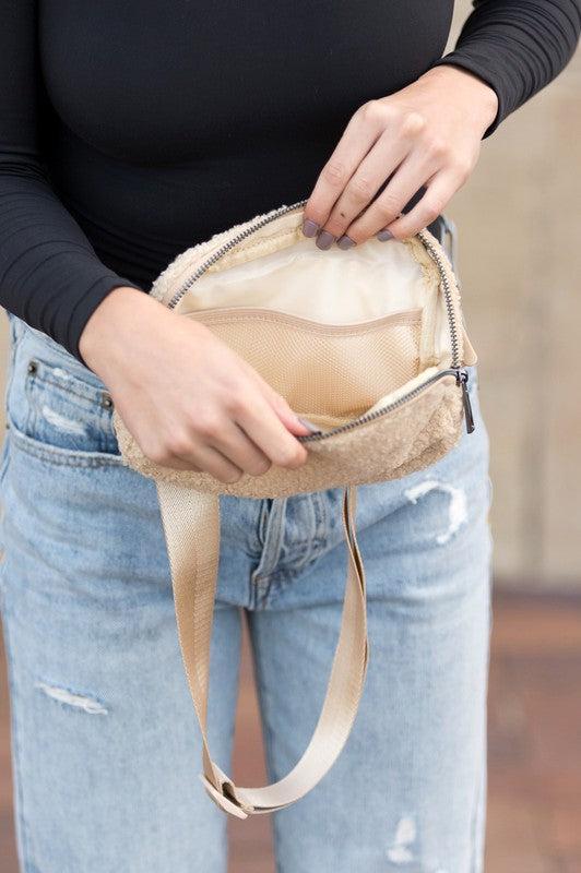 Person holding a beige crossbody bag with a blurred background