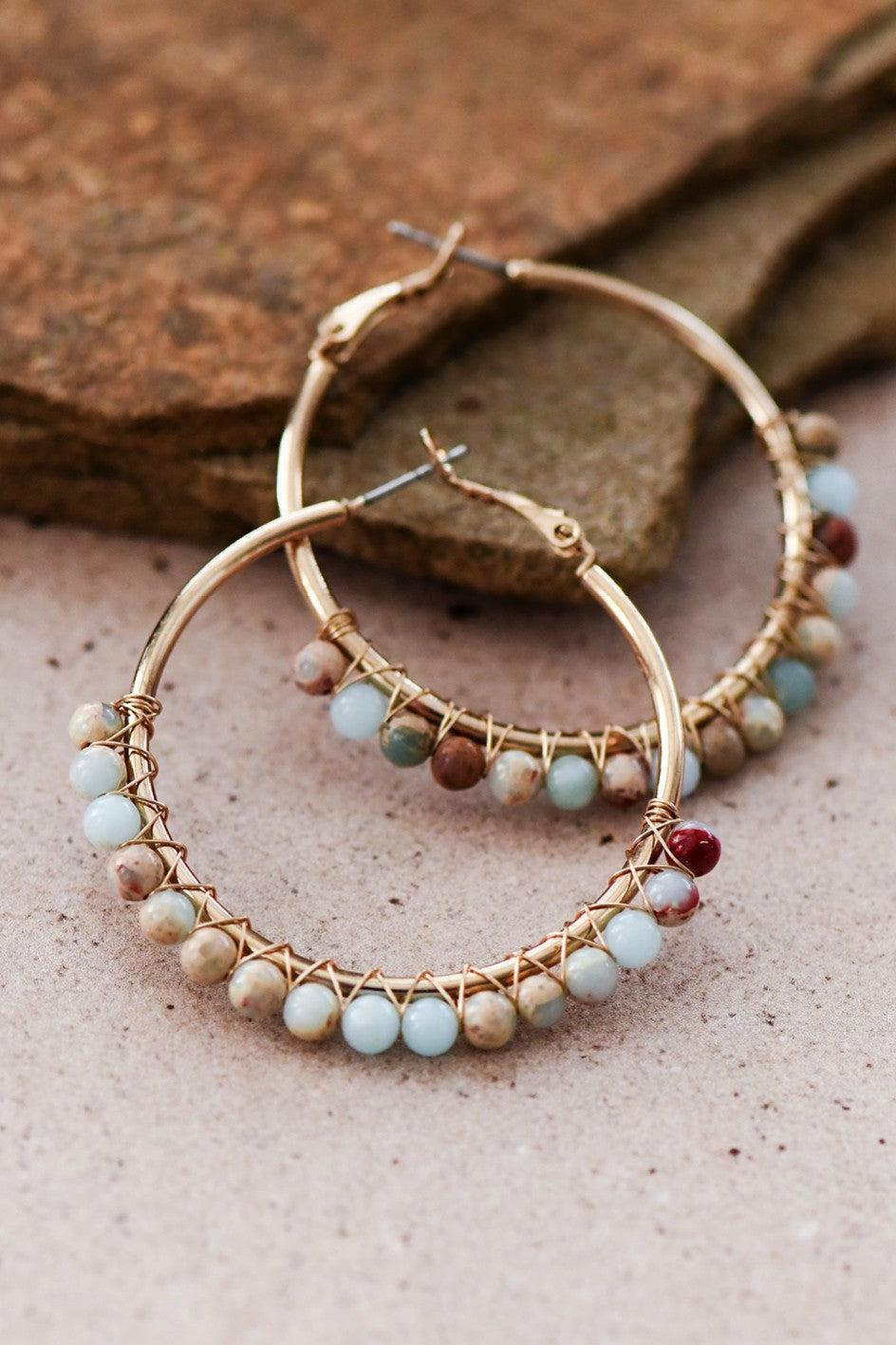 Gold hoop earrings with bead detailing on a stone surface