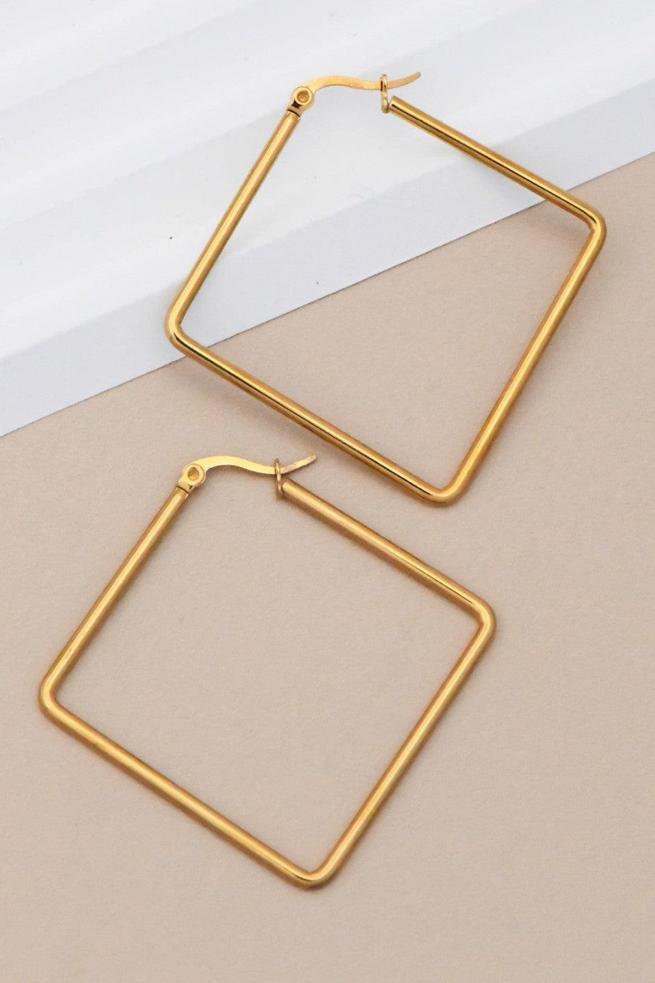 Gold square hoop earrings on a beige and white background