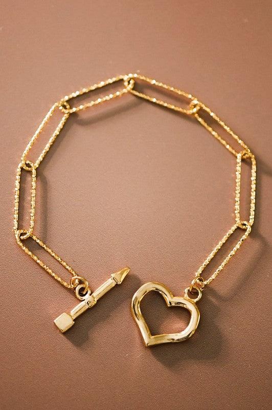 Gold bracelet with heart charm and key pendant on a brown background
