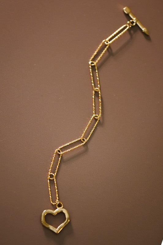 Gold chain bracelet with a heart-shaped pendant on a brown background