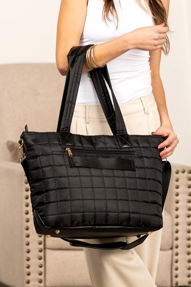 Woman holding a black nylon quilted traveler tote bag.