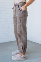 Person wearing beige high-waisted pants and light-colored shoes against a white brick wall.