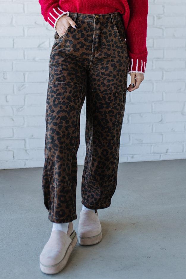 Person wearing leopard print pants and a red sweater against a white brick wall.