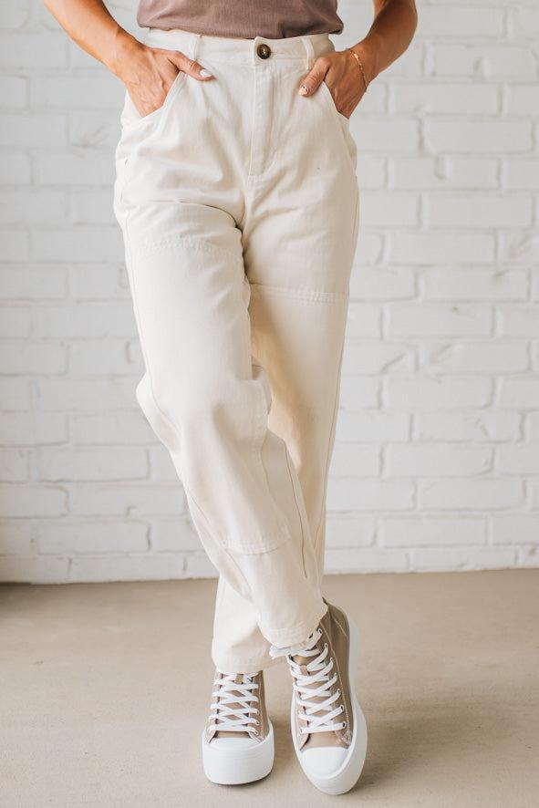 Person wearing beige pants and white sneakers against a white brick wall.