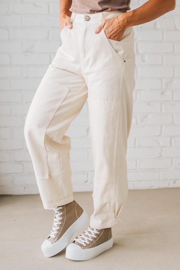 Person wearing beige pants and high-top sneakers against a white brick wall.