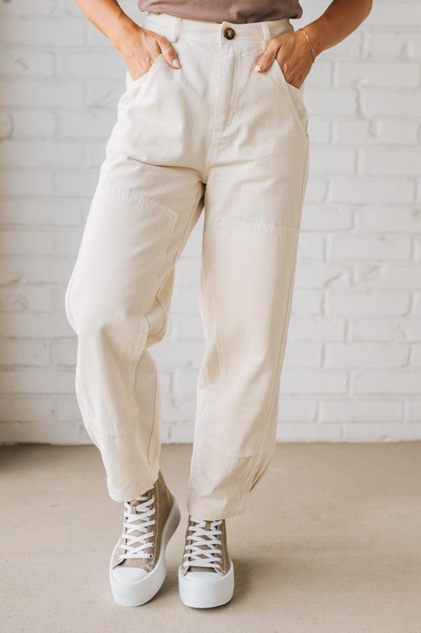 Person wearing beige pants and white sneakers against a white brick wall.