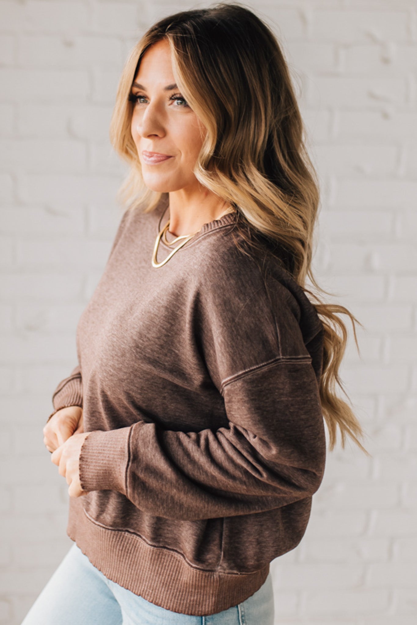 BLONDE WOMAN MODELING A LONG SLEEVE ACID WASHED PULLOVER WITH RIBBED DETAIL ON THE NECKLINE, SLEEVE CUFFS AND HEMLINE