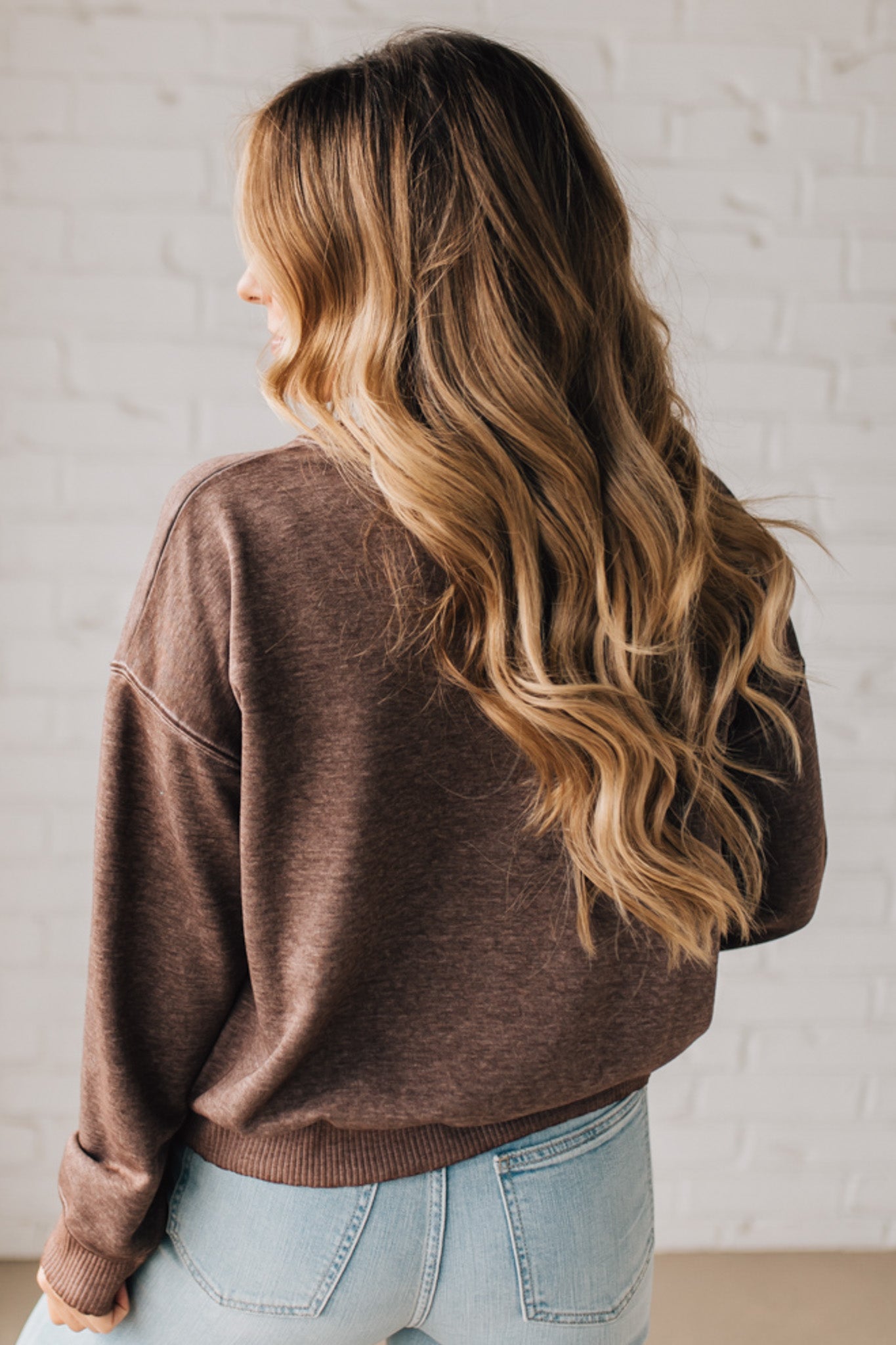 BLONDE WOMAN MODELING A LONG SLEEVE ACID WASHED PULLOVER WITH RIBBED DETAIL ON THE NECKLINE, SLEEVE CUFFS AND HEMLINE