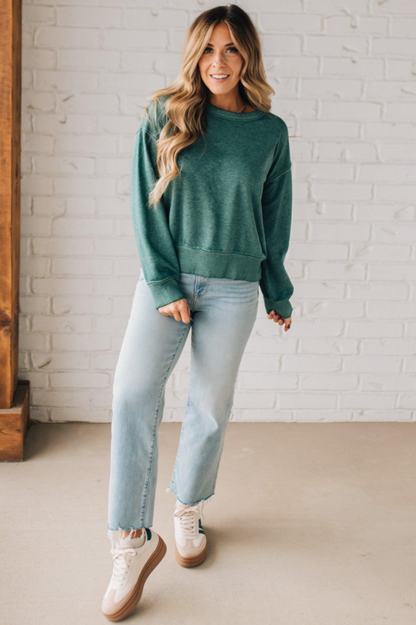 BLONDE WOMAN MODELING A LONG SLEEVE ACID WASHED PULLOVER WITH RIBBED DETAIL ON THE NECKLINE, SLEEVE CUFFS AND HEMLINE