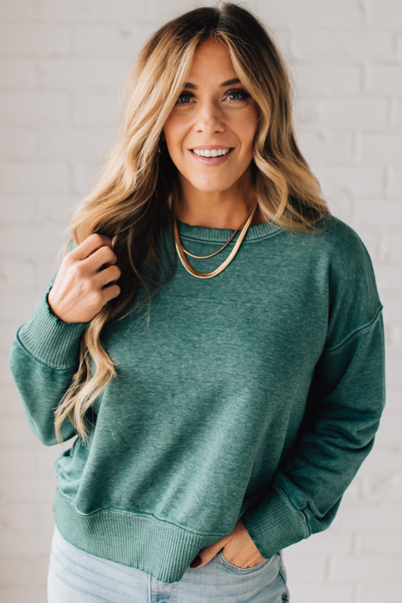 BLONDE WOMAN MODELING A LONG SLEEVE ACID WASHED PULLOVER WITH RIBBED DETAIL ON THE NECKLINE, SLEEVE CUFFS AND HEMLINE