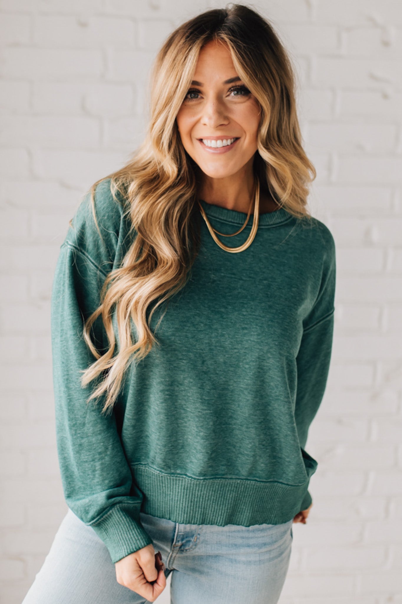 BLONDE WOMAN MODELING A LONG SLEEVE ACID WASHED PULLOVER WITH RIBBED DETAIL ON THE NECKLINE, SLEEVE CUFFS AND HEMLINE