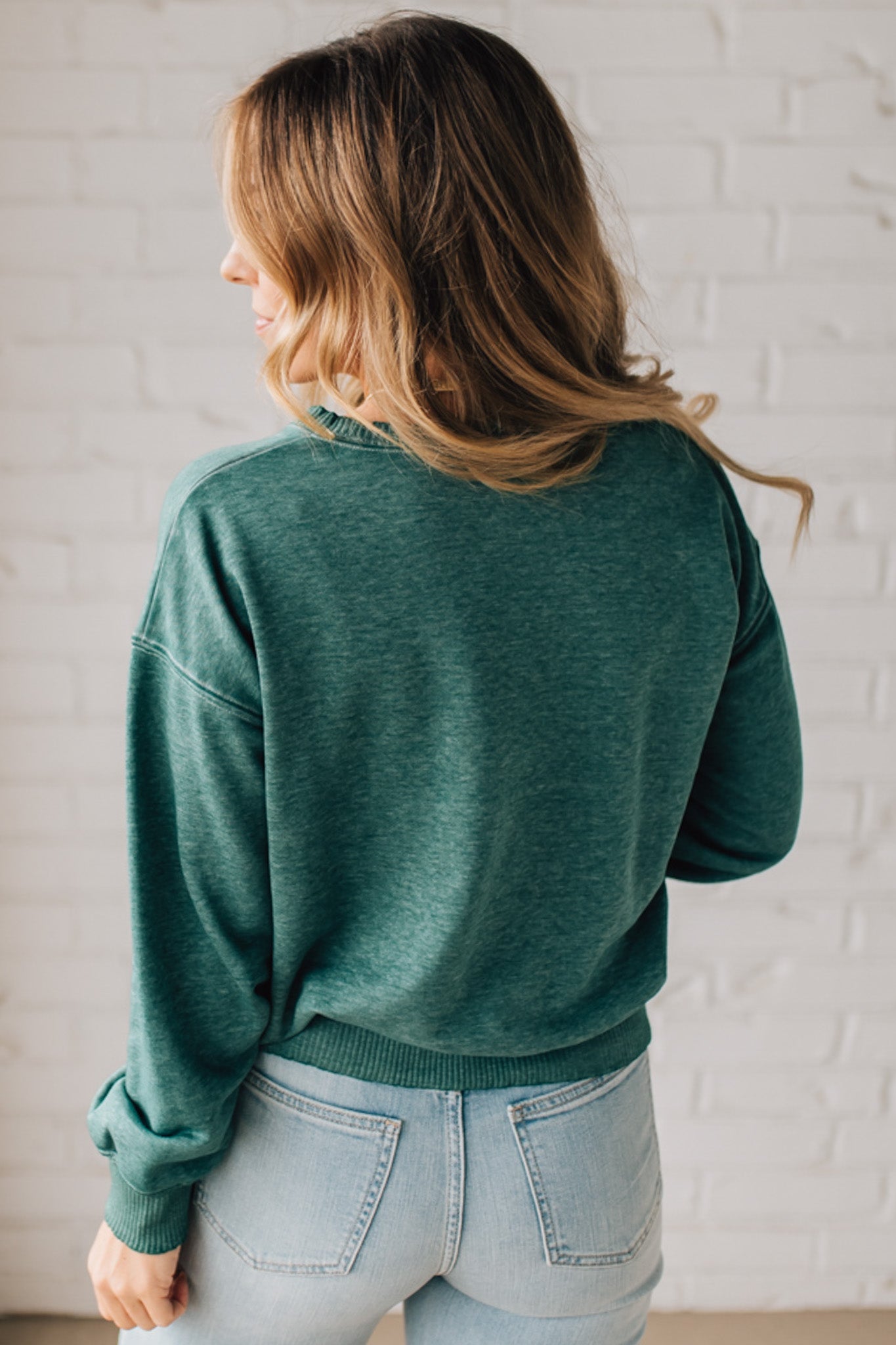 BLONDE WOMAN MODELING A LONG SLEEVE ACID WASHED PULLOVER WITH RIBBED DETAIL ON THE NECKLINE, SLEEVE CUFFS AND HEMLINE