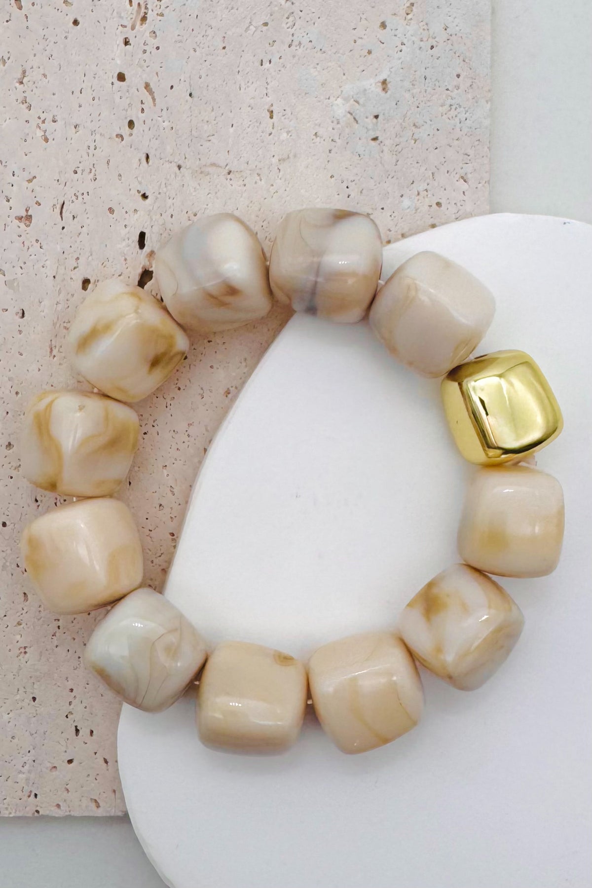 Cream bead bracelet with a gold accent bead shown on a textured surface.