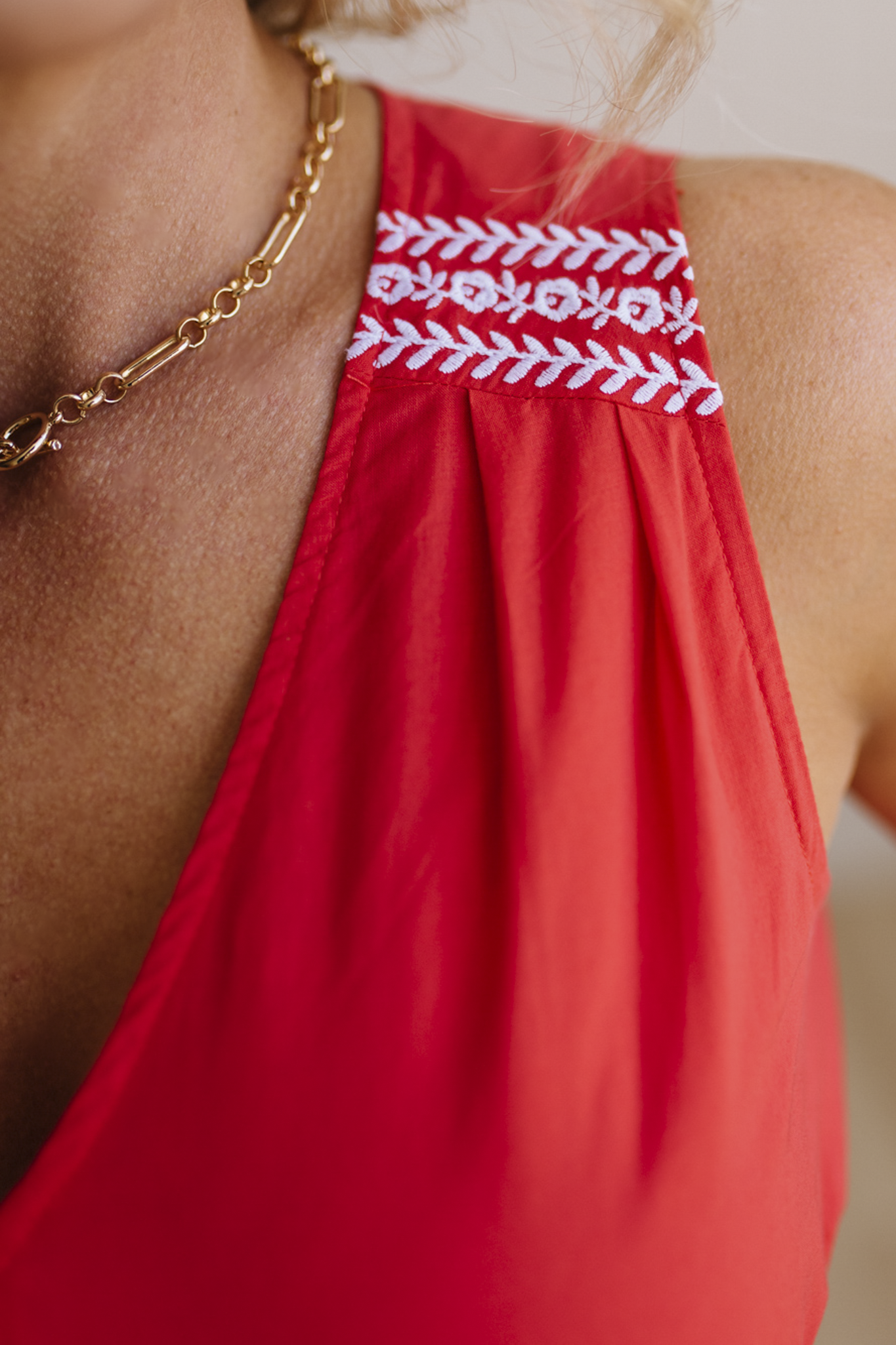Red sleeveless top with white embroidery on shoulders, worn by a person.