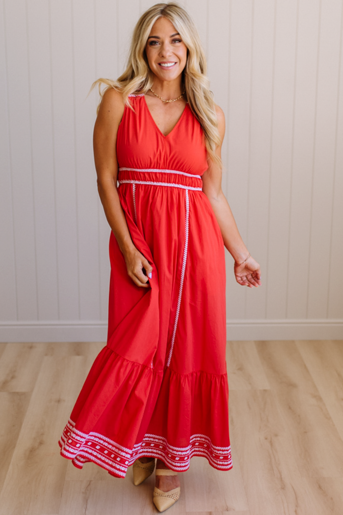 Woman wearing a red dress with white trim in a room with wooden flooring and a light-colored wall.