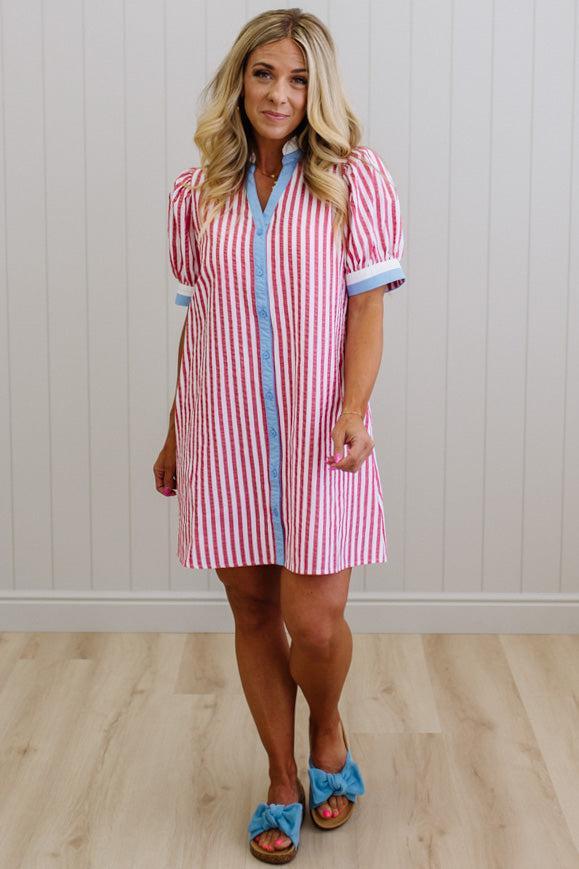 Woman wearing a red and white striped dress with blue trim against a white paneled wall.