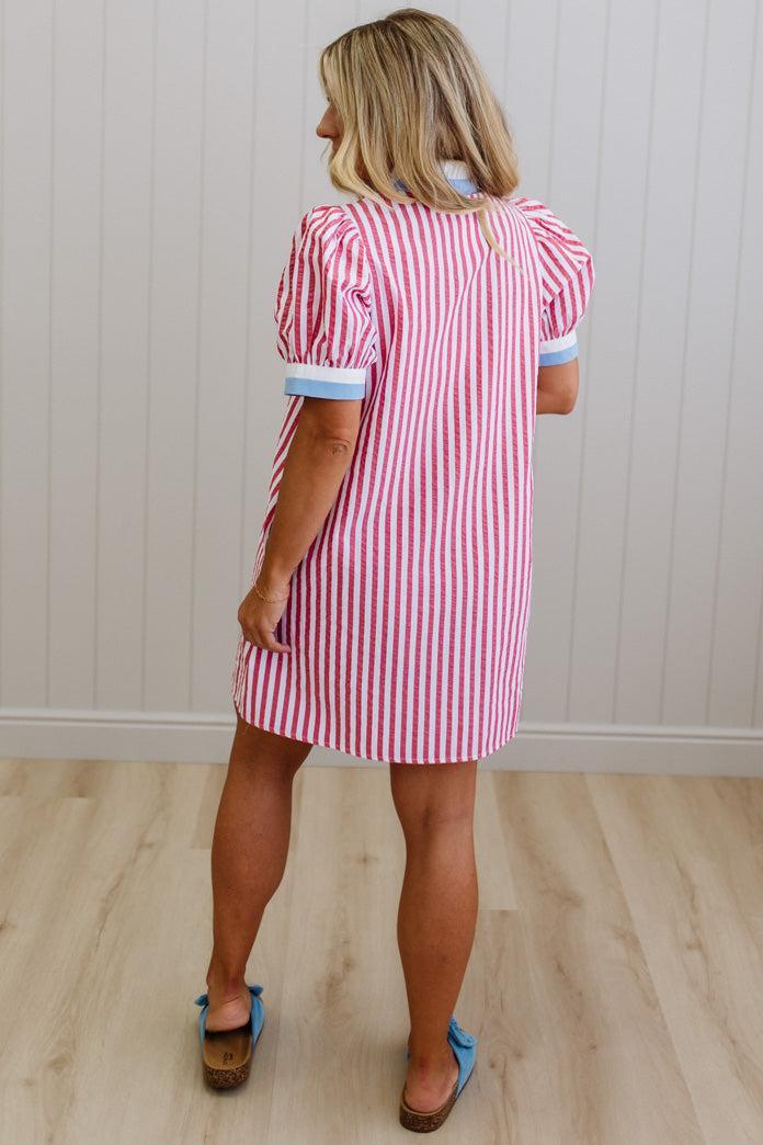 Woman wearing a red and white striped dress standing in a room with wooden flooring and a white wall.