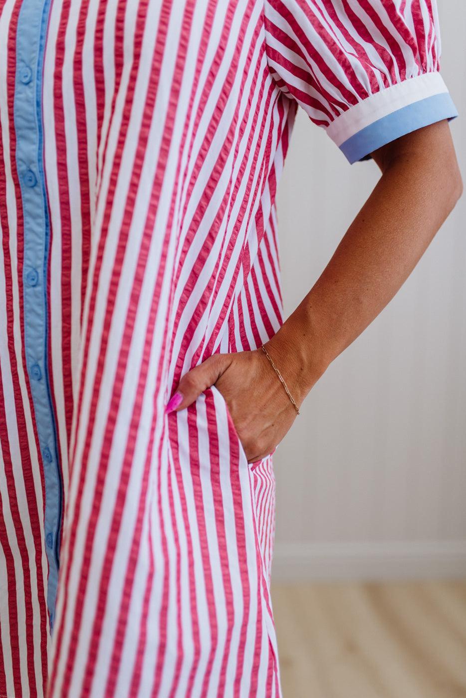 Person wearing a red and white striped dress with blue trim on a plain background
