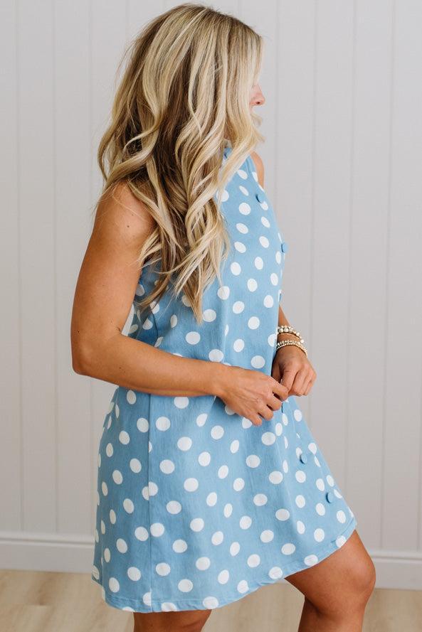 Woman wearing a blue dress with white polka dots against a neutral background