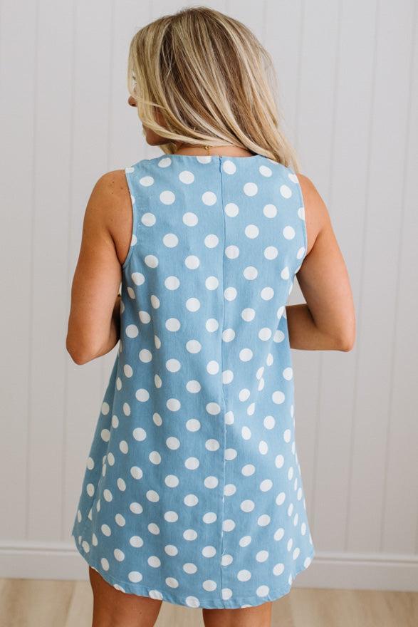 Woman wearing a blue polka dot dress against a white wall.