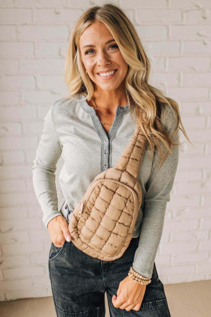 Woman holding a beige quilted bag against a white brick wall