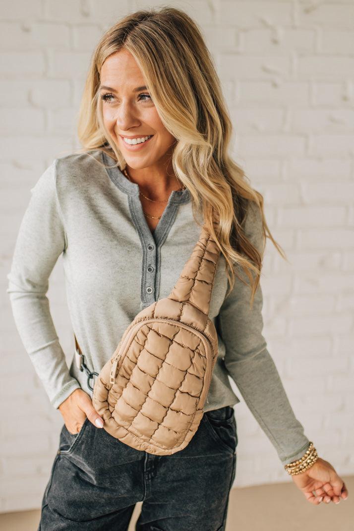 Woman holding a quilted beige bag against a white brick wall.