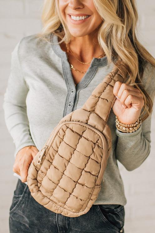 Woman holding a quilted beige handbag against a neutral background