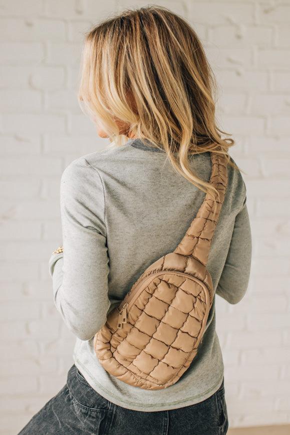Woman wearing a beige quilted crossbody bag against a light background