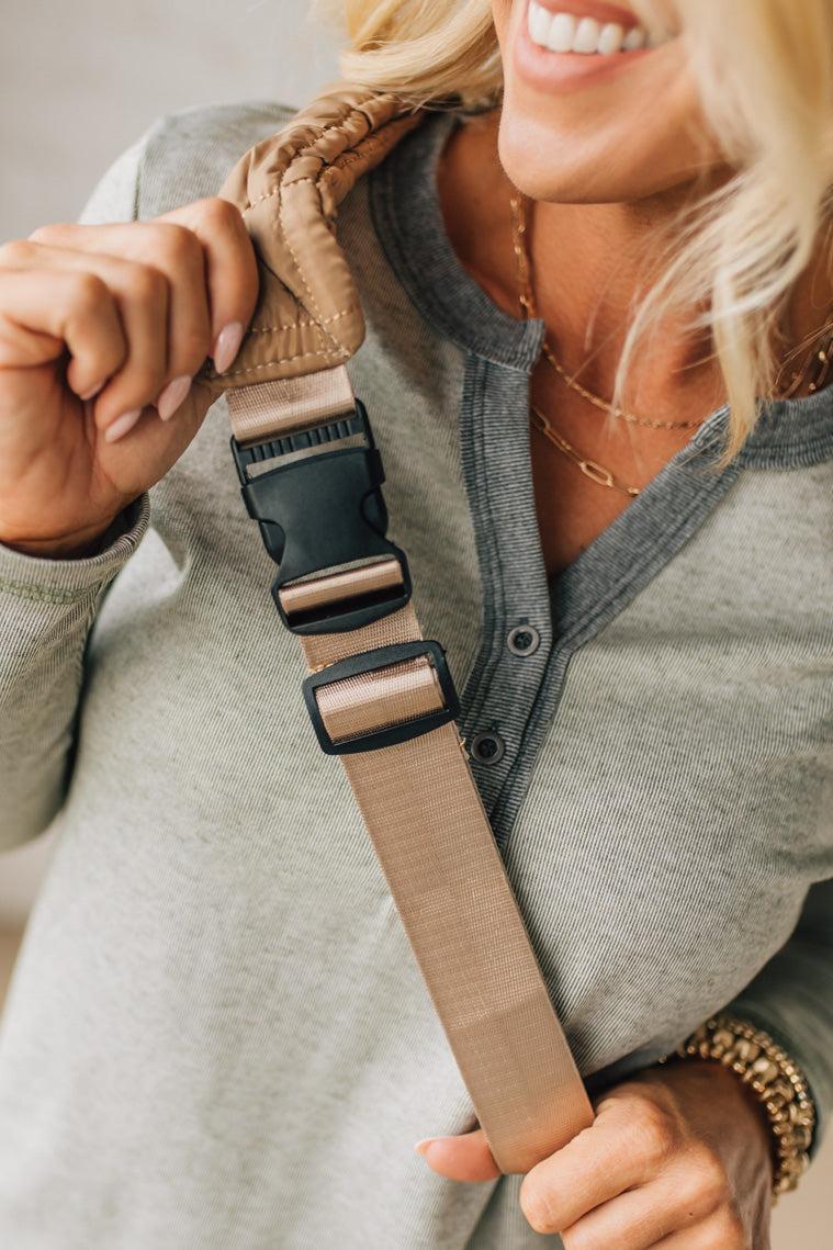 Woman holding a beige strap with a black buckle, wearing a gray hoodie.