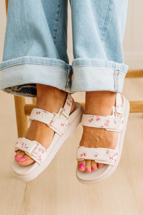 White sandals with floral pattern worn with rolled-up jeans on a neutral background