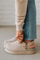 Women's beige sandals worn with blue jeans on a neutral background