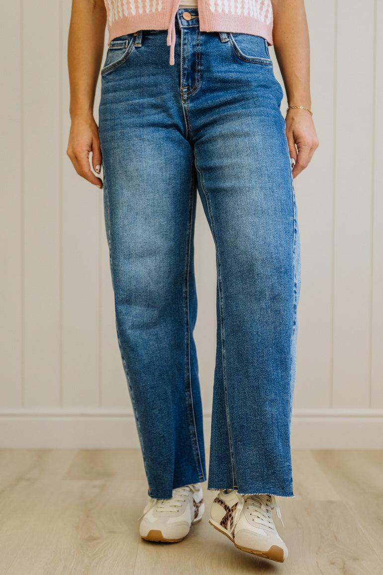 Person wearing blue jeans and white sneakers against a neutral background