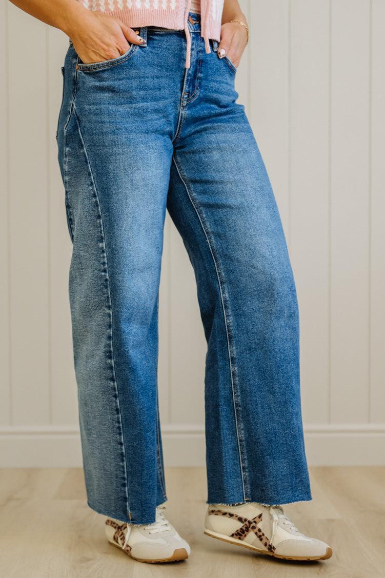 Person wearing blue jeans and white sneakers with a neutral background