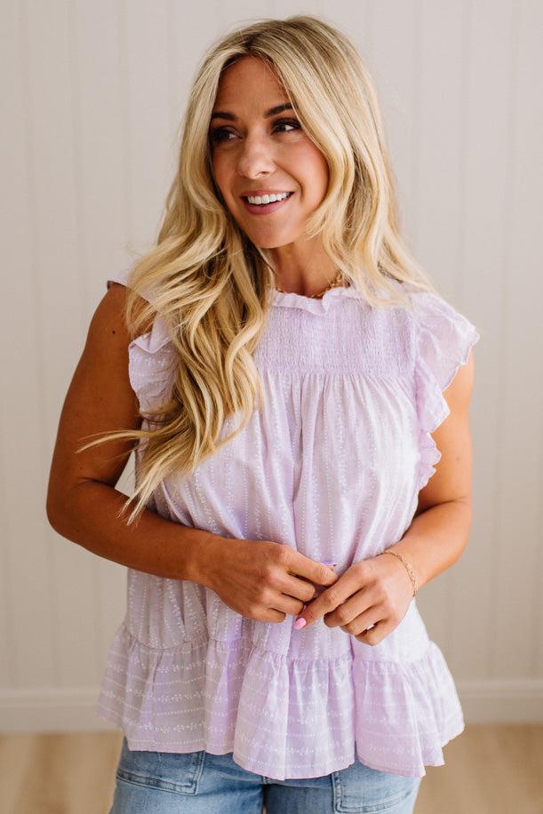 Woman wearing a light purple ruffled top and blue jeans against a plain background