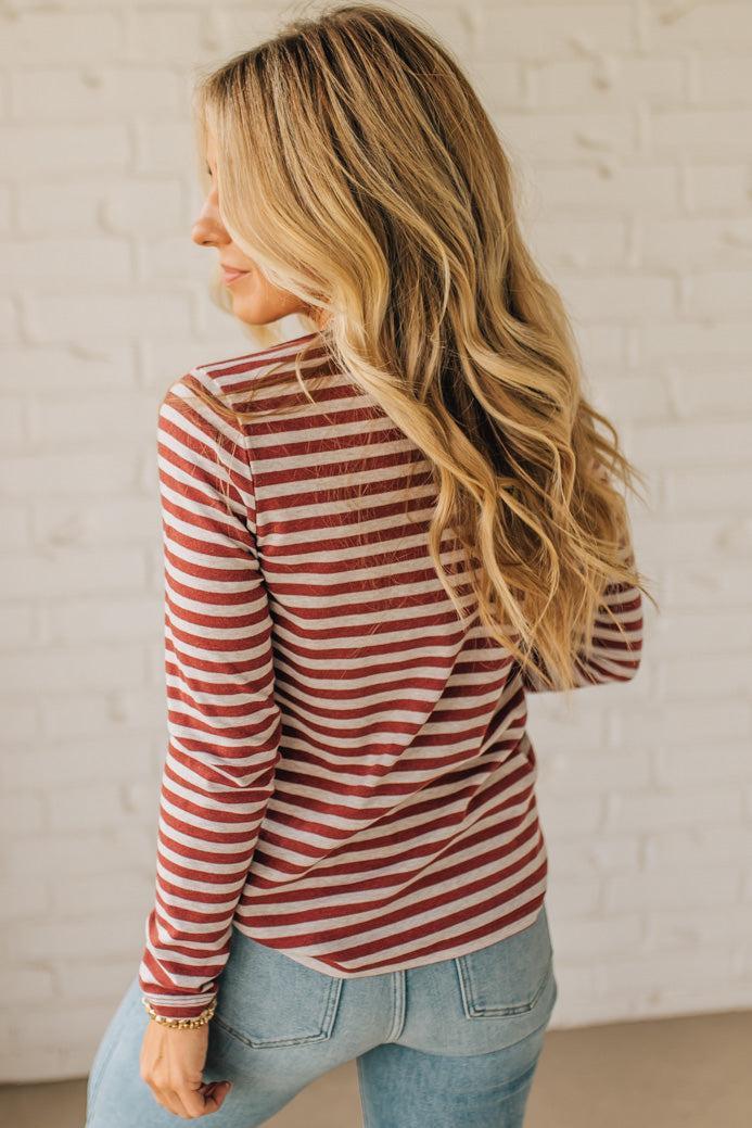 Woman wearing a red and white striped long-sleeve shirt and blue jeans against a white brick wall.