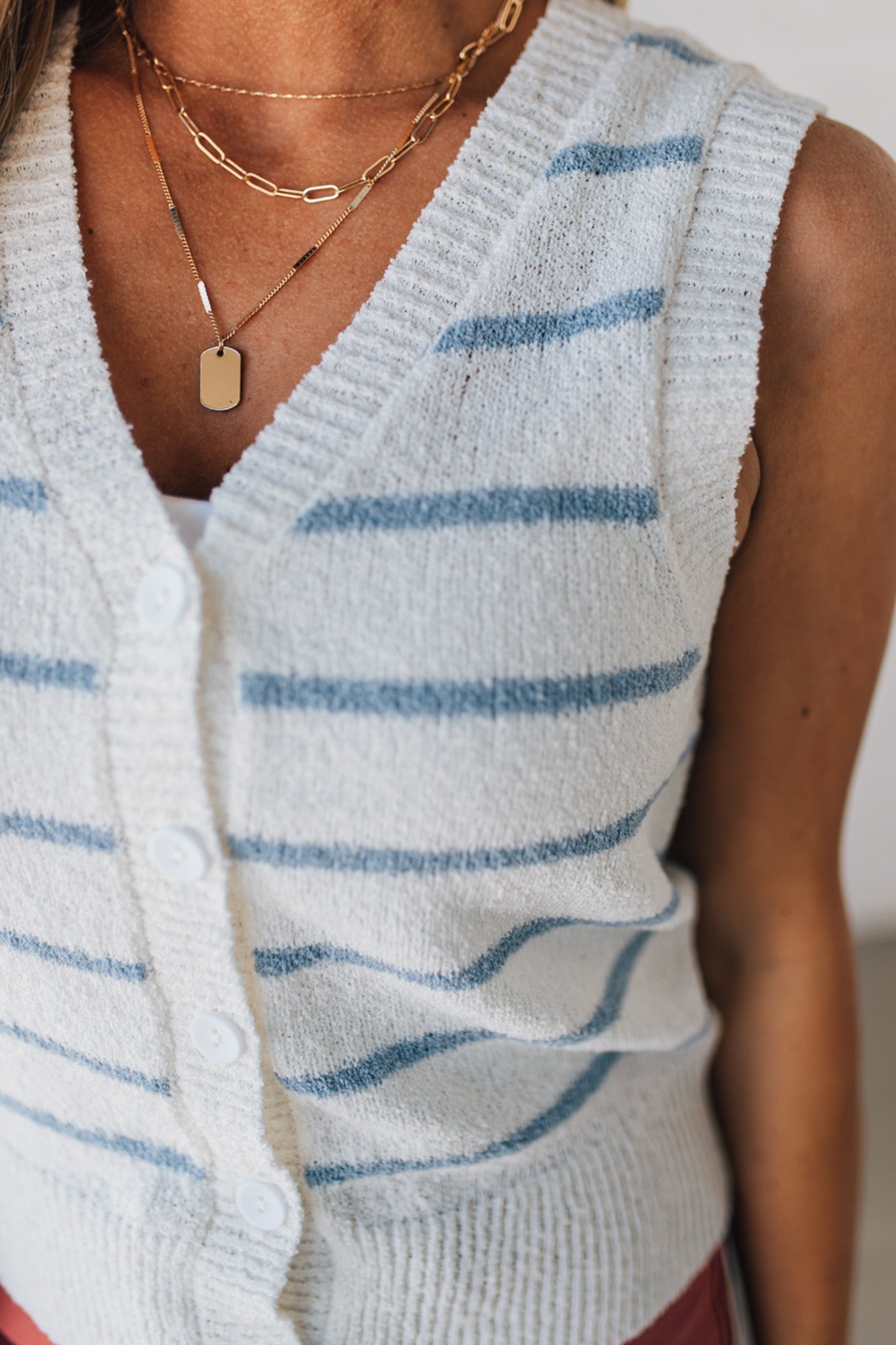 BLONDE WOMAN IN A HAT WEARING A LIGHTWEIGHT, COZY, STRIPED BUTTON UP V-NECK VEST W/ RIBBING ACCENTS THROUGHOUT BODY.
