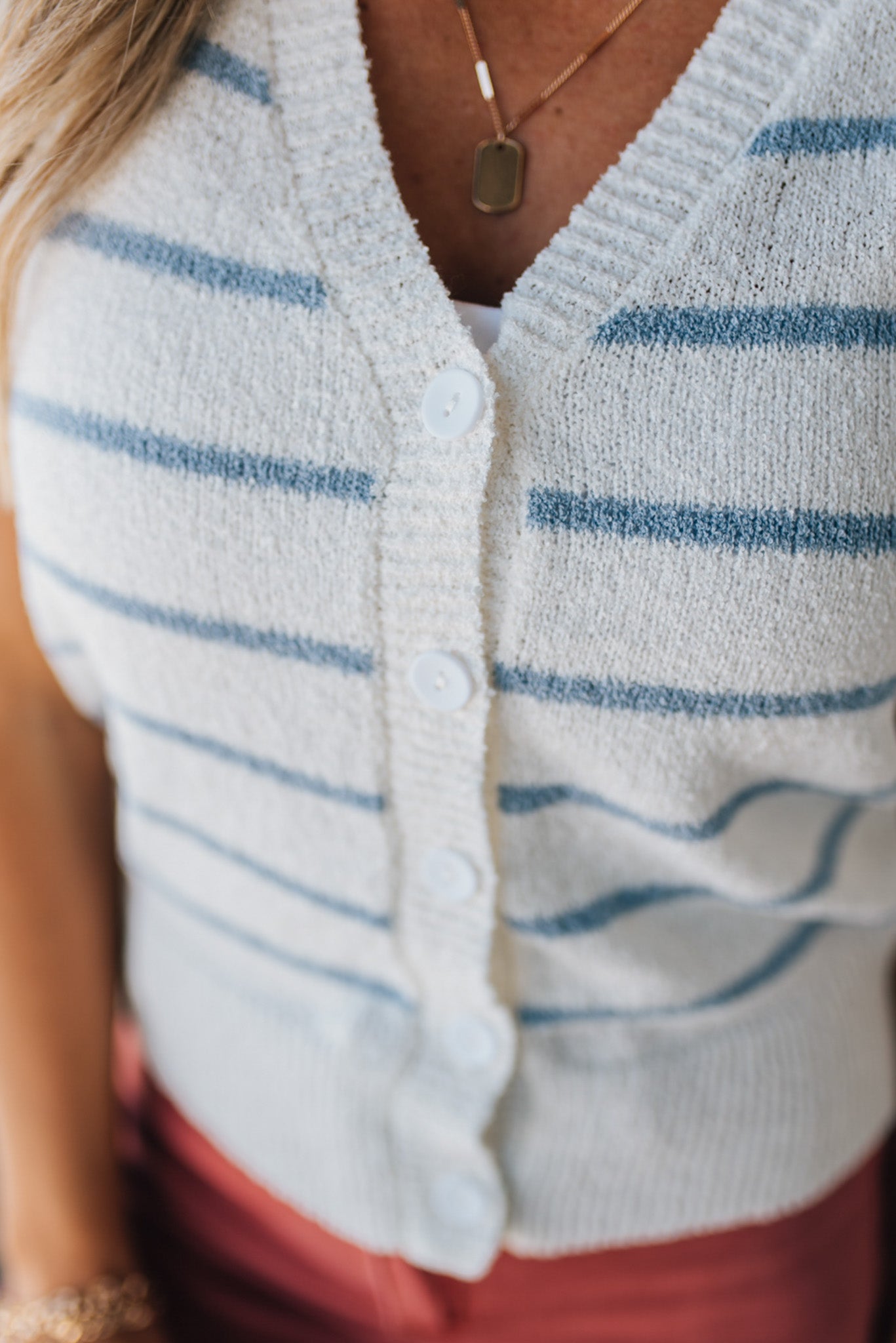 BLONDE WOMAN IN A HAT WEARING A LIGHTWEIGHT, COZY, STRIPED BUTTON UP V-NECK VEST W/ RIBBING ACCENTS THROUGHOUT BODY.
