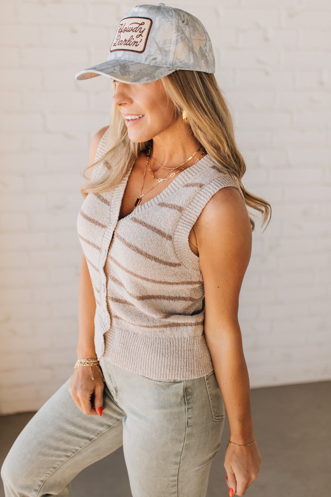 BLONDE WOMAN IN A HAT WEARING A LIGHTWEIGHT, COZY, STRIPED BUTTON UP V-NECK VEST W/ RIBBING ACCENTS THROUGHOUT BODY.