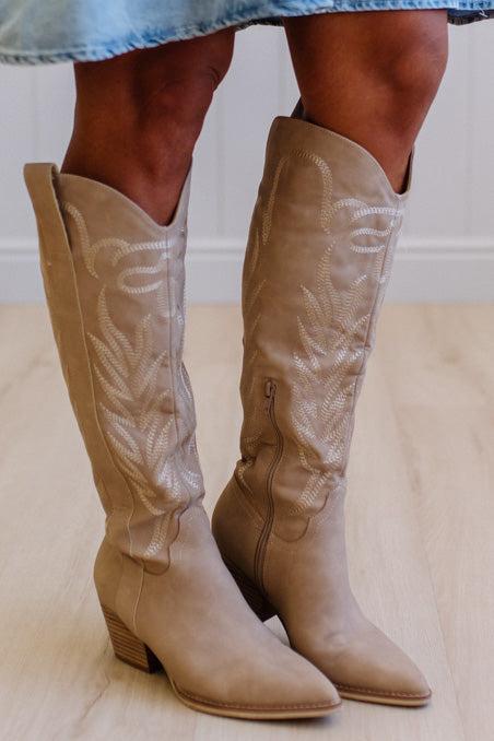 Beige knee-high boots worn by a person on a light wooden floor.