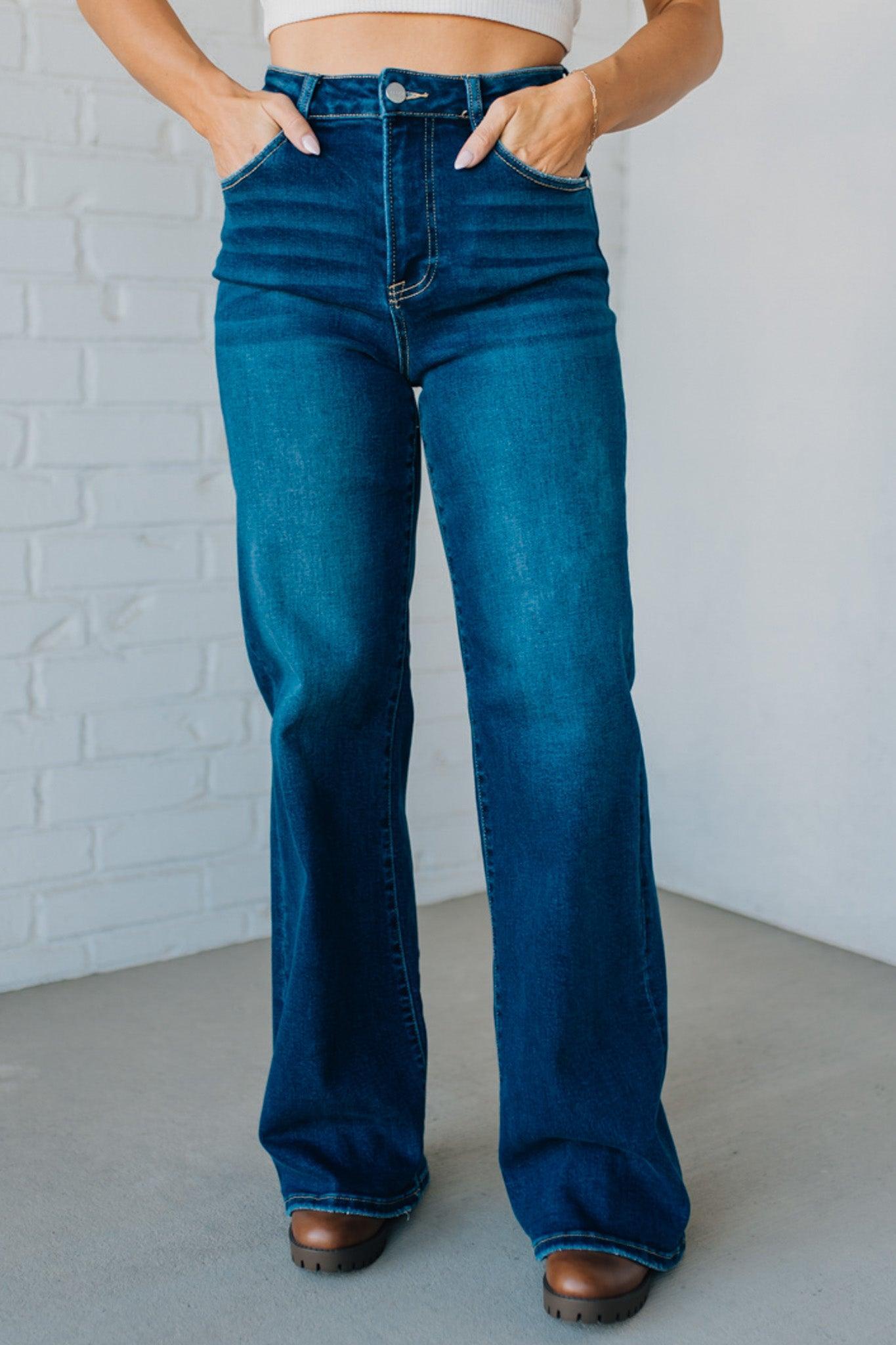 Person wearing blue flared jeans against a white brick wall.