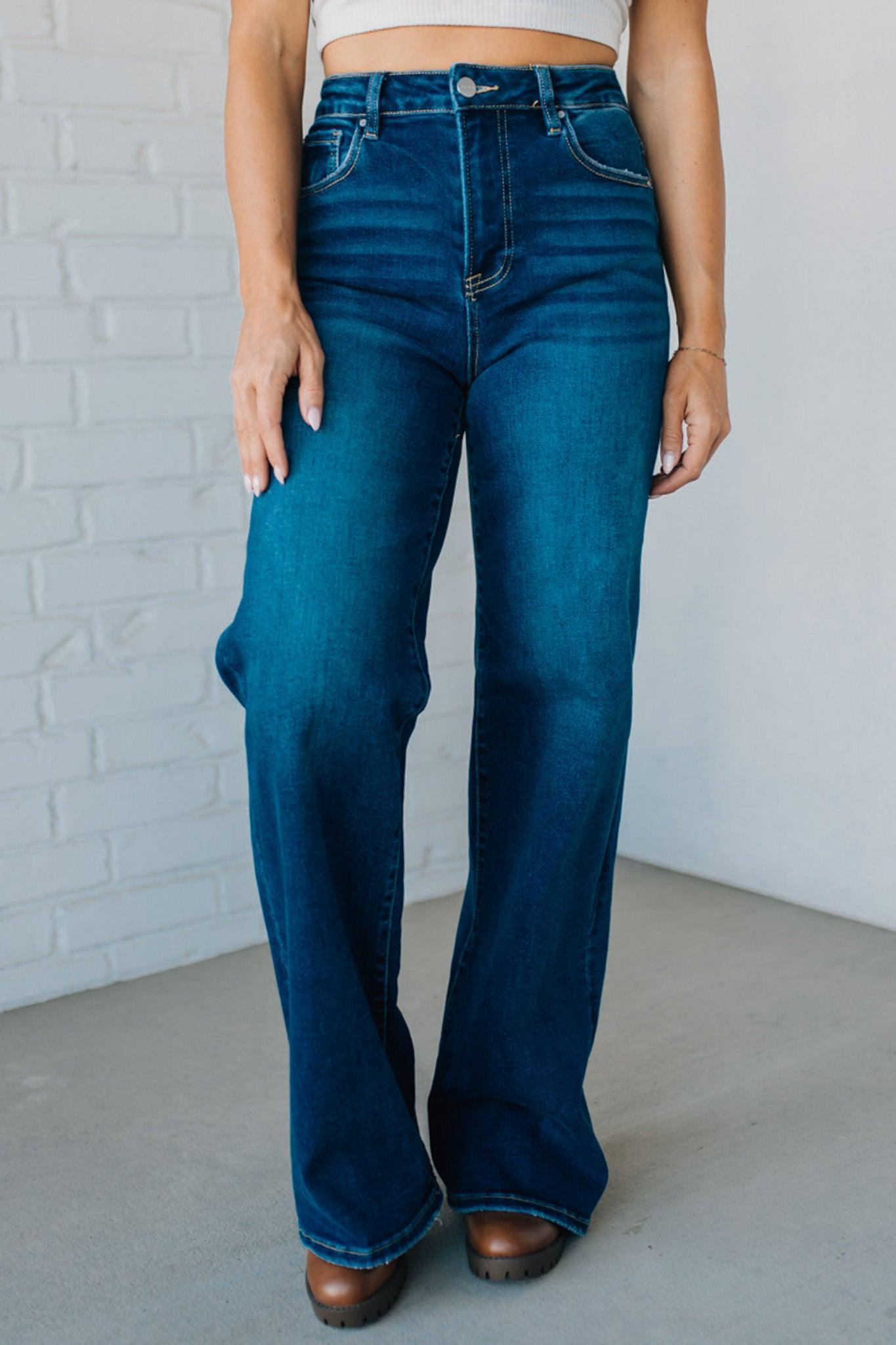 Person wearing blue jeans standing against a white brick wall.