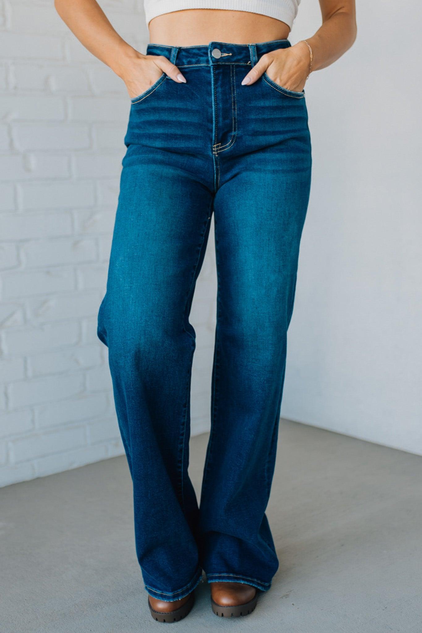 Person wearing blue flared jeans against a white brick wall.