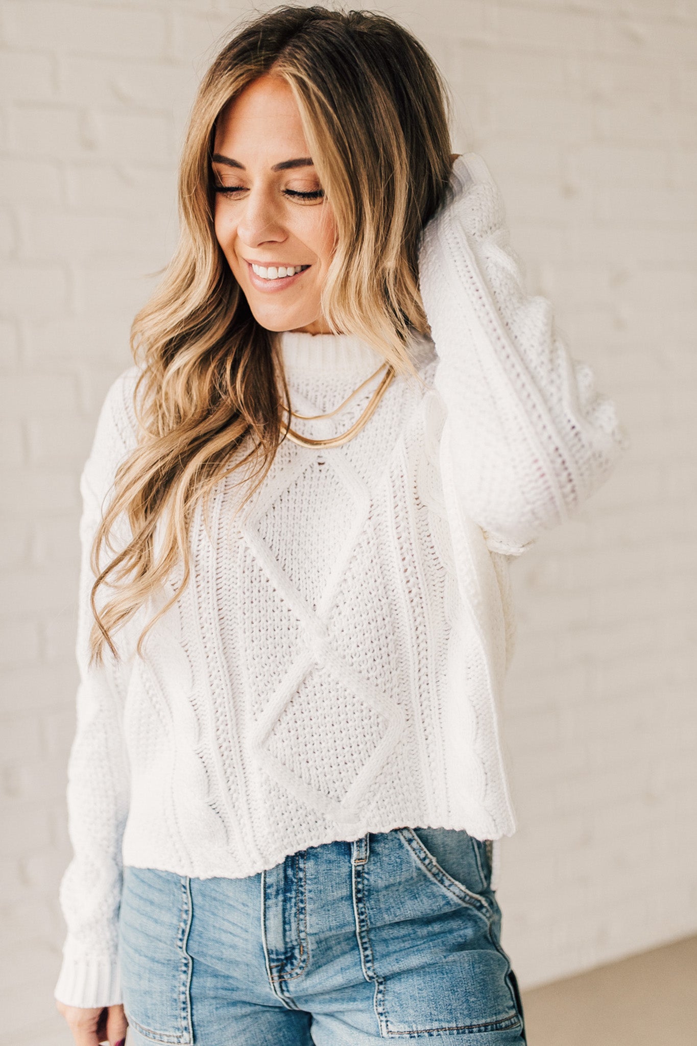 Blonde girl modeling a white long sleeve cable knit sweater