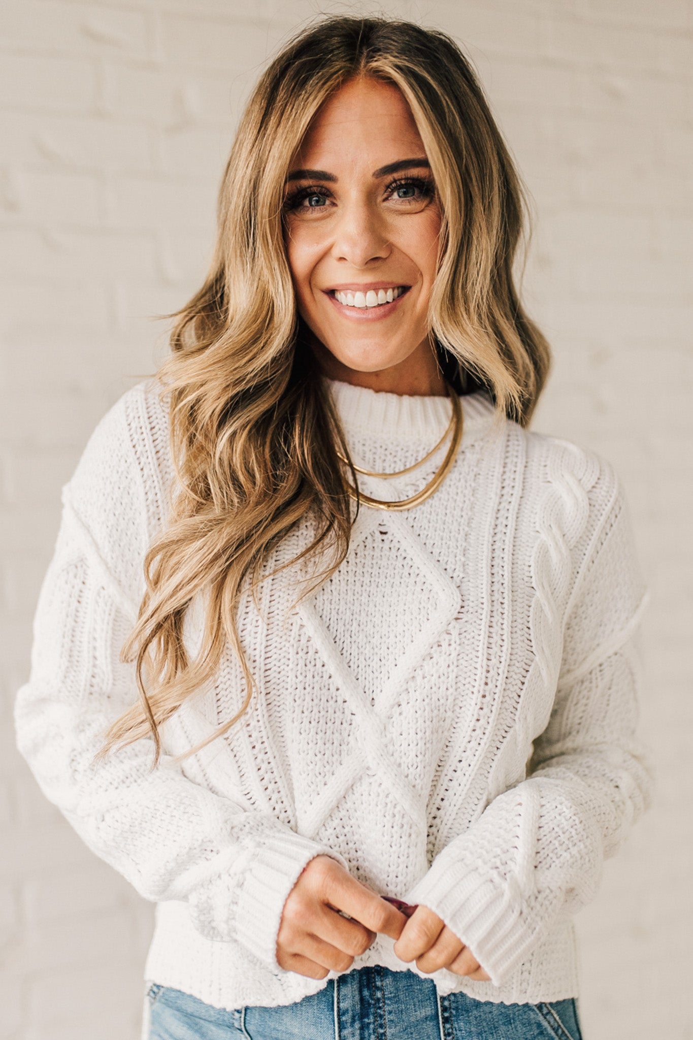 Blonde girl modeling a white long sleeve cable knit sweater