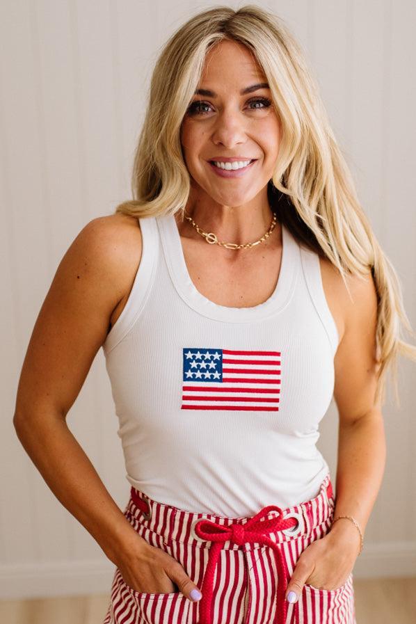 Woman wearing a white tank top with an American flag design and red and white striped pants.