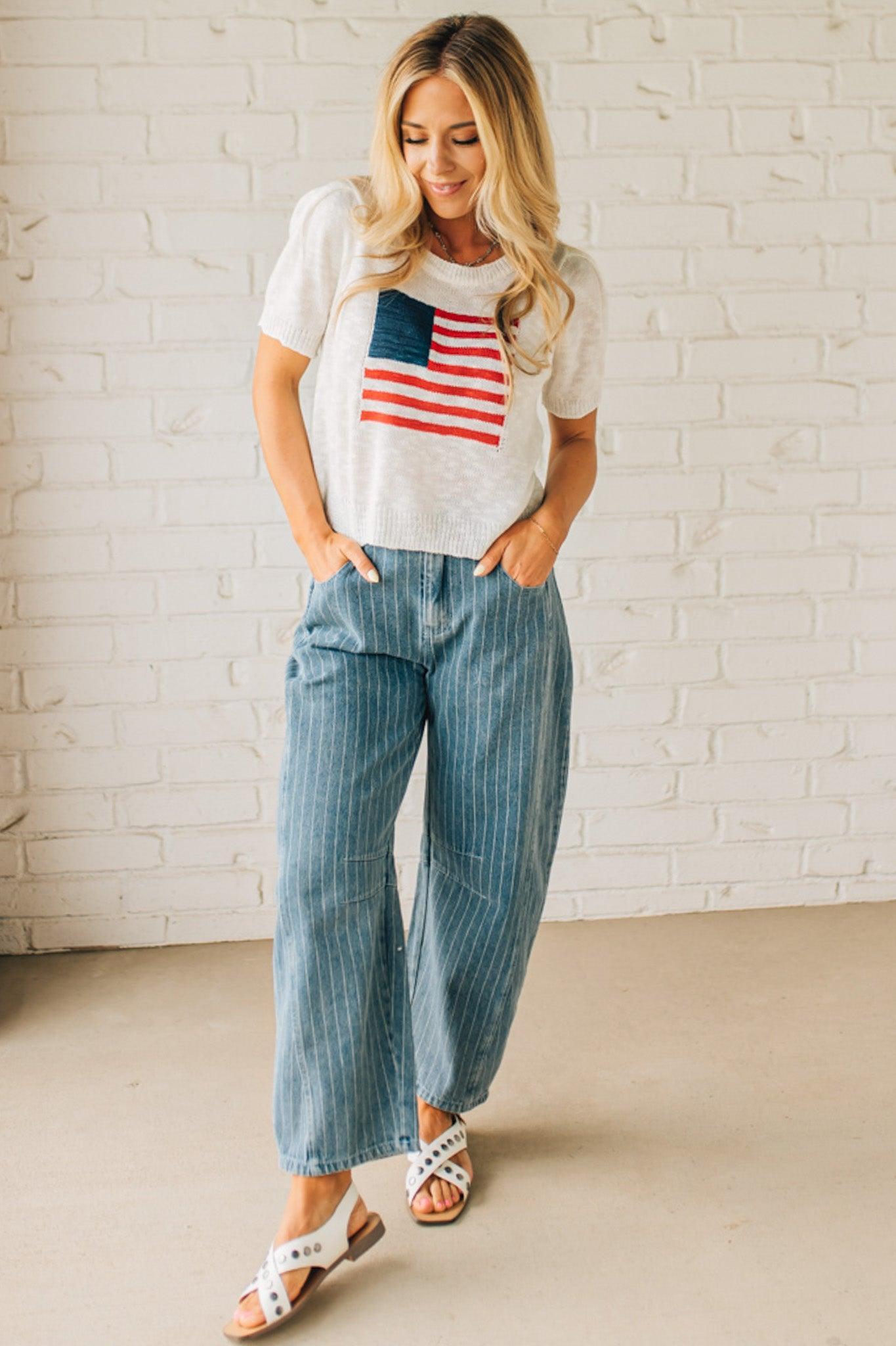 BLONDE WOMAN WEARING A WHITE AMERICAN FLAG TOP WITH SHIRRING DETAILS SHORT SLEEVES SWEATER TOP.