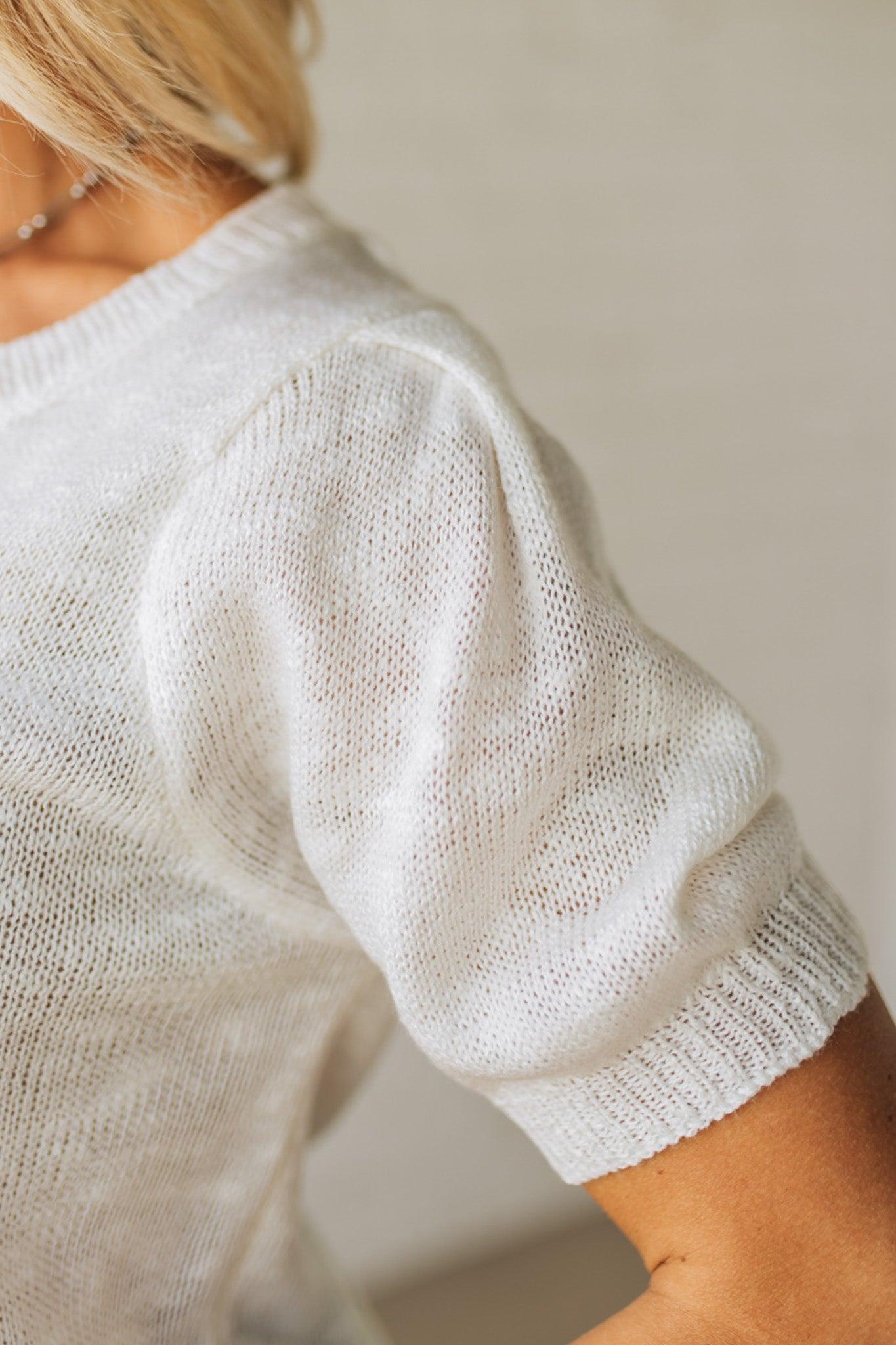 BLONDE WOMAN WEARING A WHITE AMERICAN FLAG TOP WITH SHIRRING DETAILS SHORT SLEEVES SWEATER TOP.
